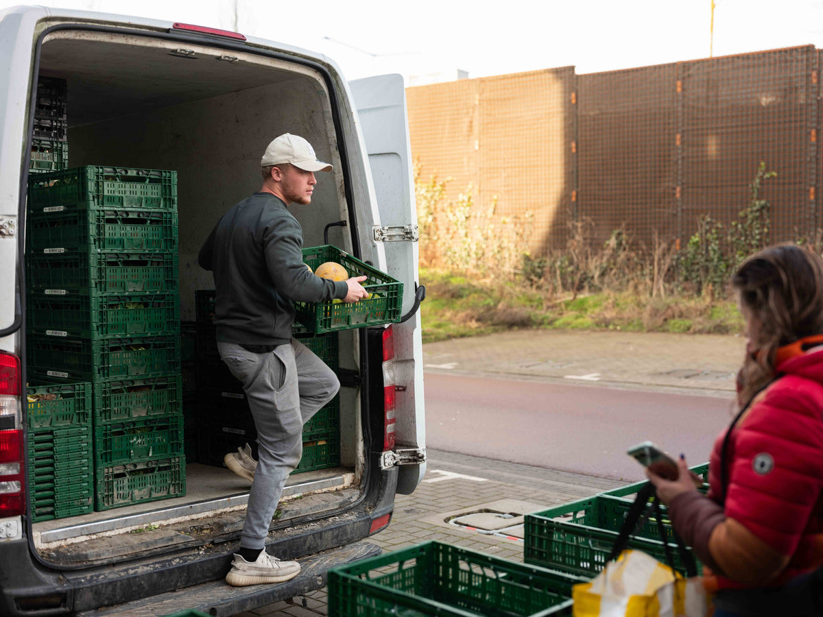 Een Veggiebox-medewerker stapt met een krat uit de bus terwijl een klant bij het afhaalpunt wacht